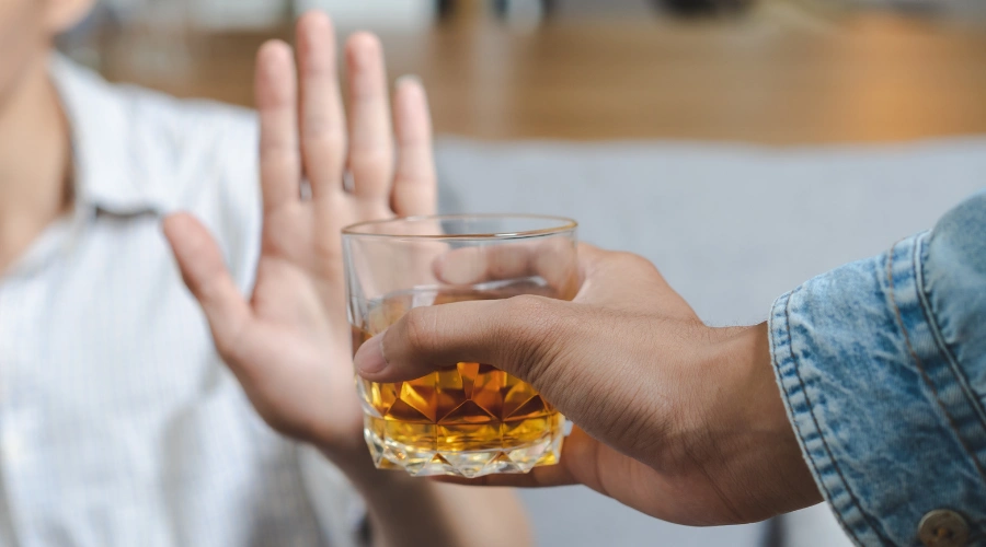 Image of the palm of a man's hand held in a stop motion next to a someone providing a glass of whiskey - Alcohol Tapering - Icarus Recovery Center