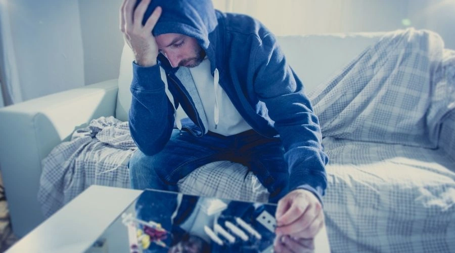 man sitting on sofa with hand on head looking depressed - Causes of Active Addiction and Drug Use