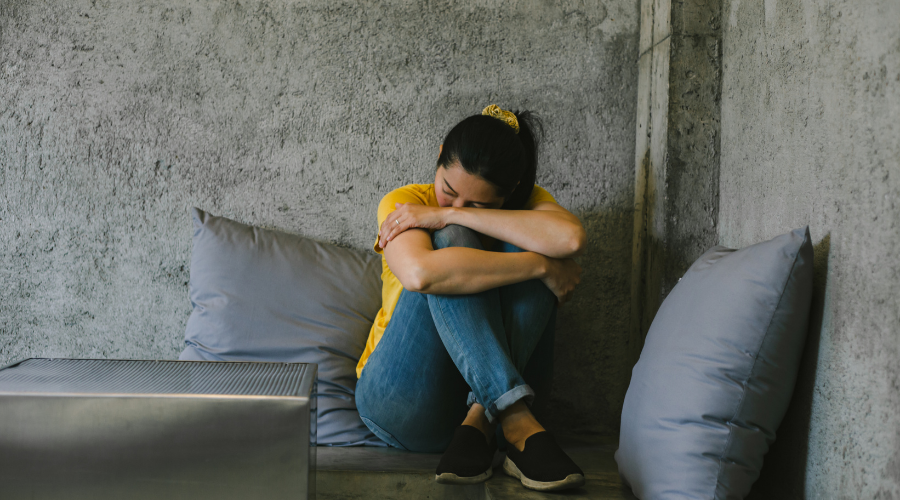 Woman sitting on a sofa with here face on her knees displaying a Connection Between Trauma and Memory Loss