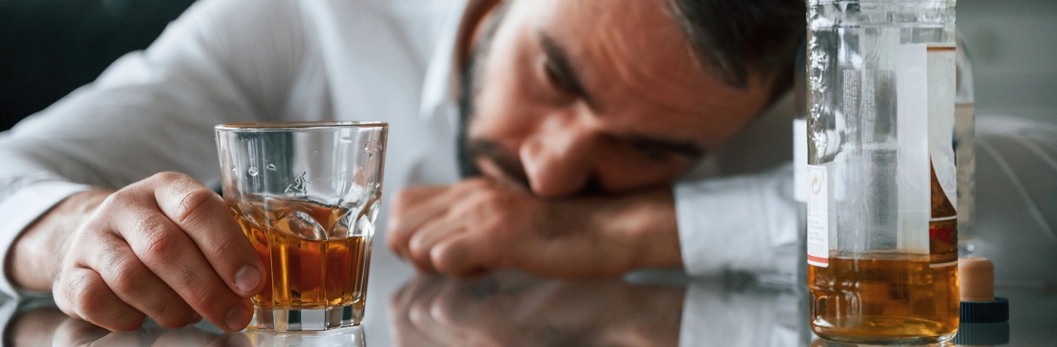 Man with head on table beside a glass of whiskey - Does Heavy Drinking Cause Prostate Problems - Icarus Recovery Center