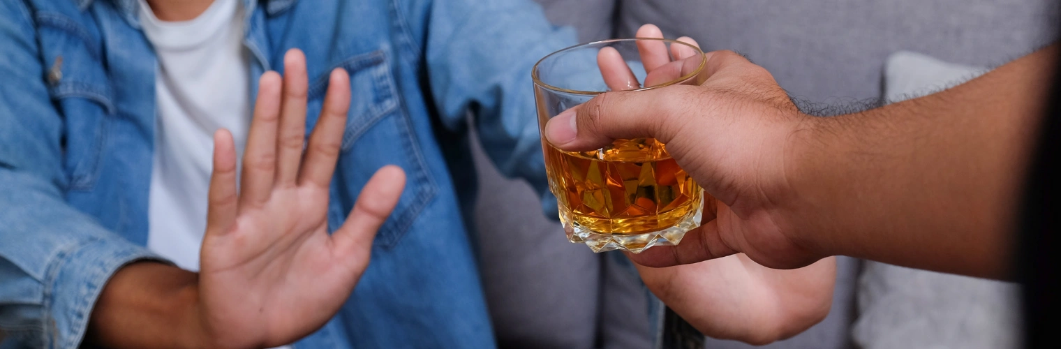 Image of a person holding a glass of whiskey with a person on the the other side holding hand up to stop - How to Wean Off Alcohol - Icarus Recovery Center