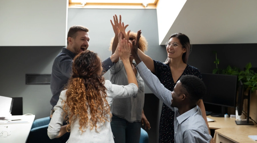 Men and women in group therapy high-fiving each other - Living with PTSD as a Disability - Supportive Co-Workers