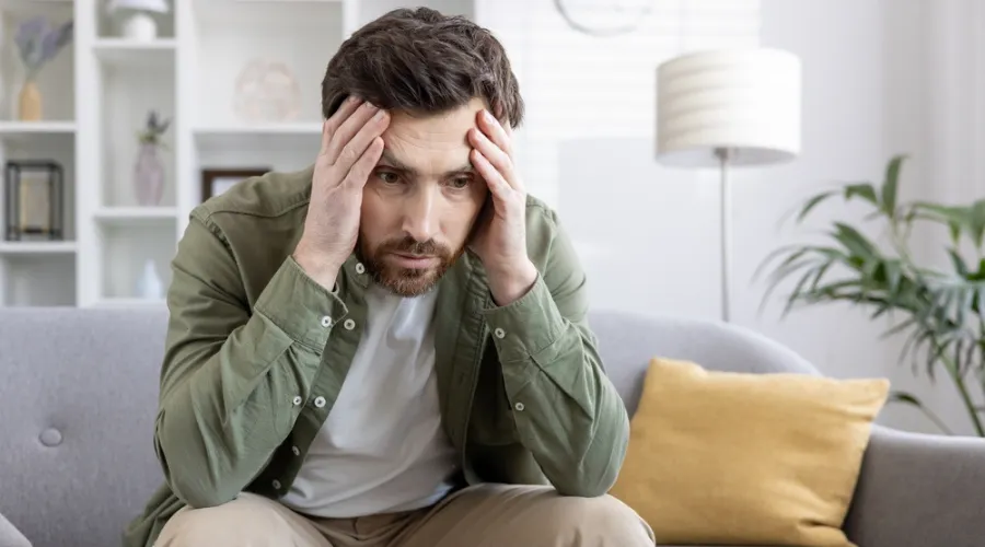 Man sitting alone on a sofa with hands on his forehead looking disturbed - Memory Loss and PTSD - Memory Loss Caused by Trauma