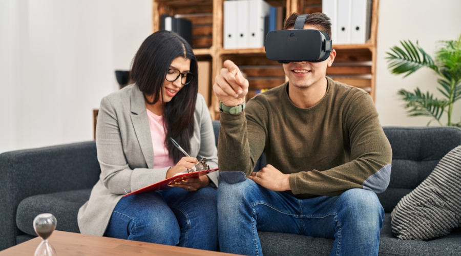Man sitting in treatment smiling a wearing video display glasses with counselor beside him - Traumatic Memory Loss Treatment at Icarus Recovery Center