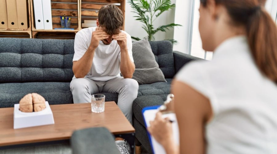 Patient with hands on his eyes sitting with a counselor taking notes - What is a Psychological Evaluation
