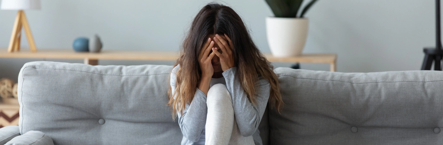 Image of depressed woman covering face and crying, sitting on couch - Symptoms of Complex PTSD - Icarus NM