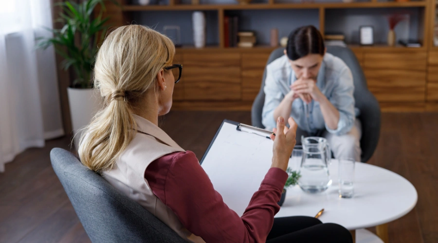 Image of female psychologist sitting in armchair, talking with upset female patient