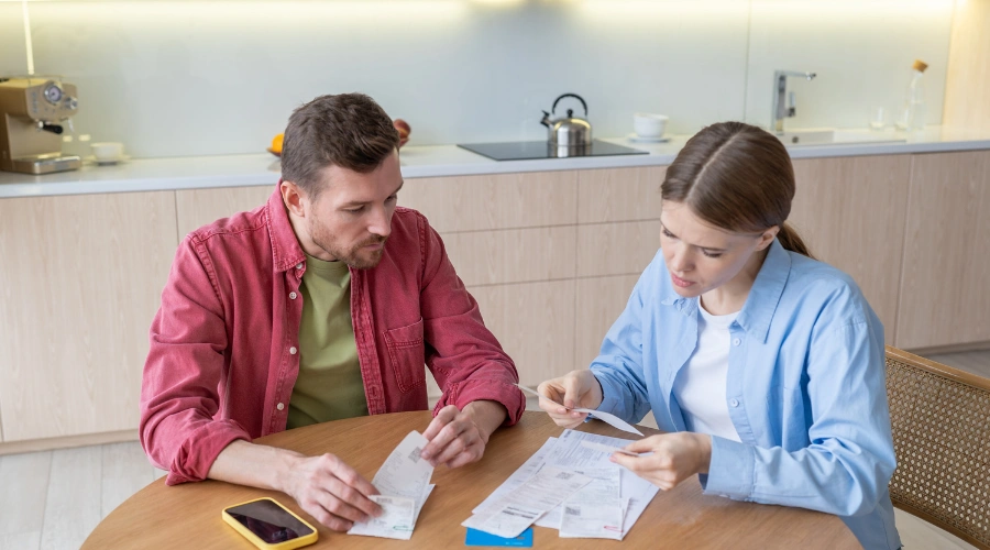 Image of a couple looking stressed at a table with bills and finances, highlighting financial strain caused by addiction