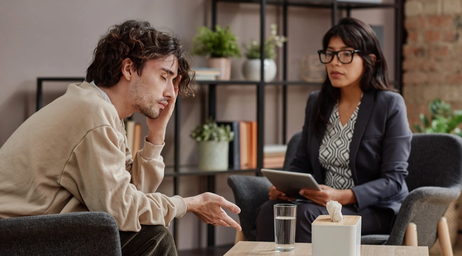 Image of a man sitting in a therapy session, reflecting on his addiction and receiving guidance to improve his marriage